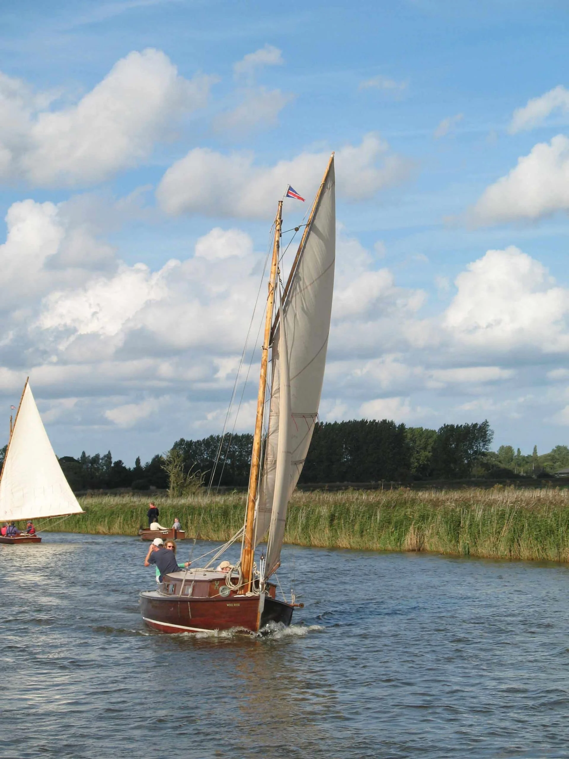 Lucent, a Lullaby class cabin yacht, sailing down one of the Norfolk Broad's rivers.