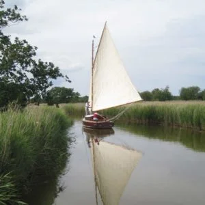 Hustler 5 meandering down a quiet river. A traditional wooden Norfolk Broads cabin yacht.